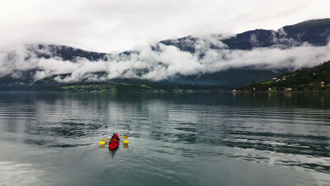 paddle boat on a big blue lake with high mountains and clouds in the background, norway, nature, drone