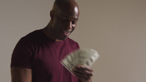 studio shot of excited mature man celebrating winning cash prize holding handful of 100 dollar bills