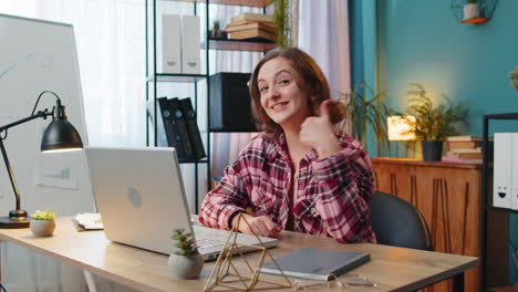 business woman looking approvingly at camera showing thumbs up sign like positive feedback at home