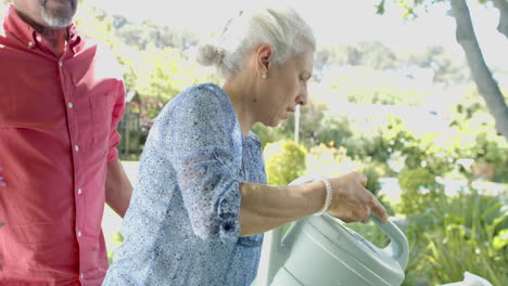 Feliz-Pareja-Birracial-De-Ancianos-Trabajando-Y-Regando-Plantas-En-Un-Jardín-Soleado-En-Casa,-Cámara-Lenta