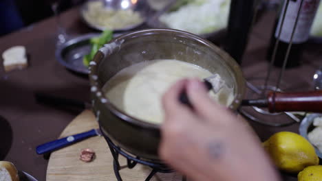 creamy pot of bagna cauda sits at the center of a rustic table as one fork dips meat and another pasta, highlighting the piedmontese tradition of communal dipping in garlic-anchovy sauce.