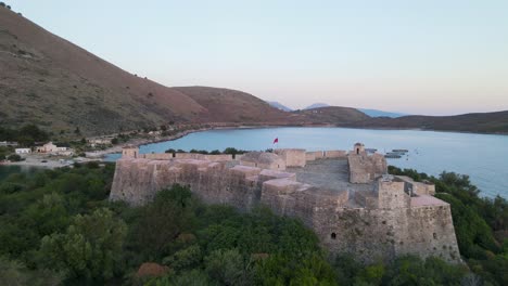 Aerial view of Porto Palermo&#039;s majestic castle on the coast, framed by mountains and the ocean, in a captivating sunset scene