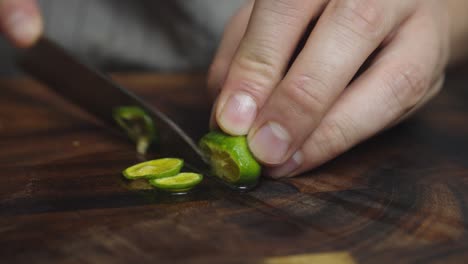 slicing green lime lemon with kitchen knife on wooden cut board