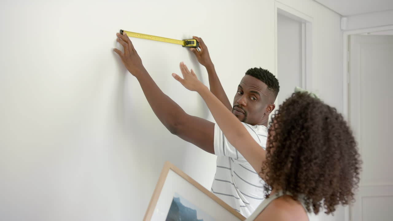 Measuring wall with tape measure, couple planning to hang picture frame