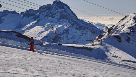 Unrecognizable-skier-using-t-bar-ski-lift-up-the-slope-with-mountain-scenery-on-a-sunny-day