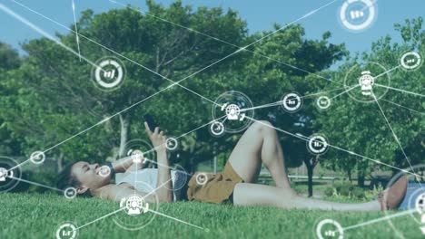 animation of network of connections with technological icons over woman using smartphone lying on gr