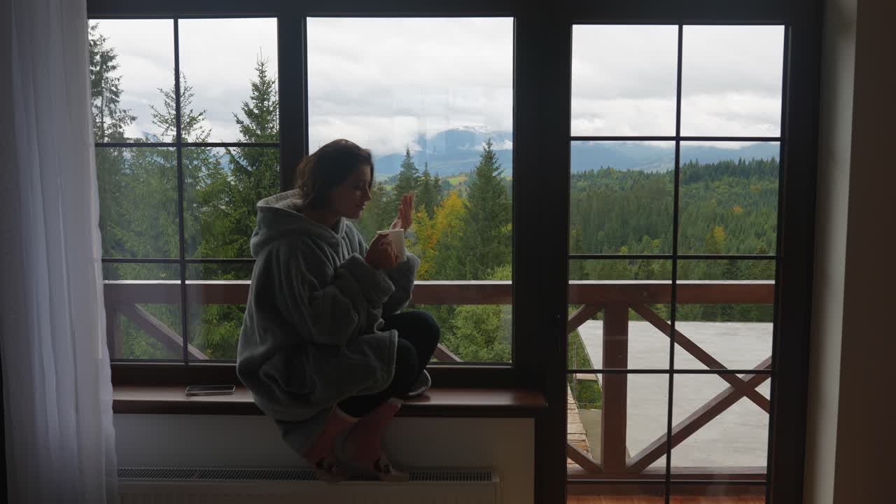 Donna che si gode un caffè vicino alla finestra con vista sulle montagne