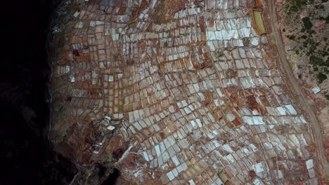 Aerial,-top-down,-drone-shot-above-a-salt-pools,-at-a-mine,-Salineras,-in-the-Andes-mountains,-cloudy-day,-in-Peru,-South-America