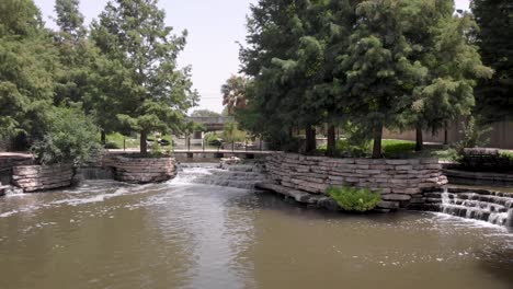 waterfalls and shade trees make for a pleasant stroll on the san antonio riverwalk, in san antonio, texas