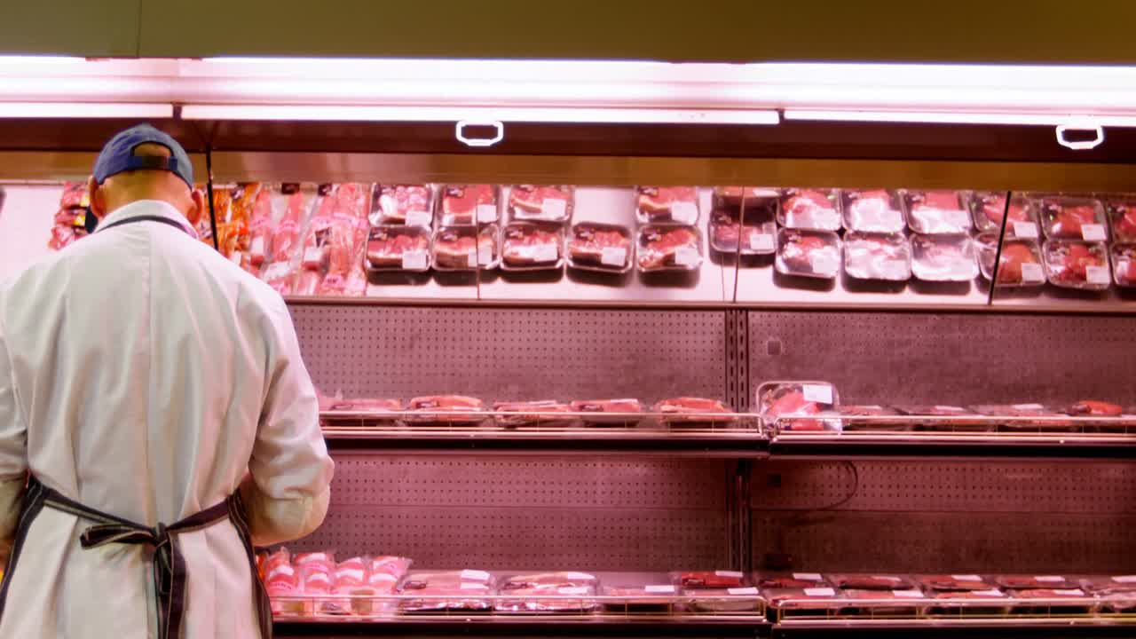 macellaio che organizza la carne avvolta in rack al negozio 4k