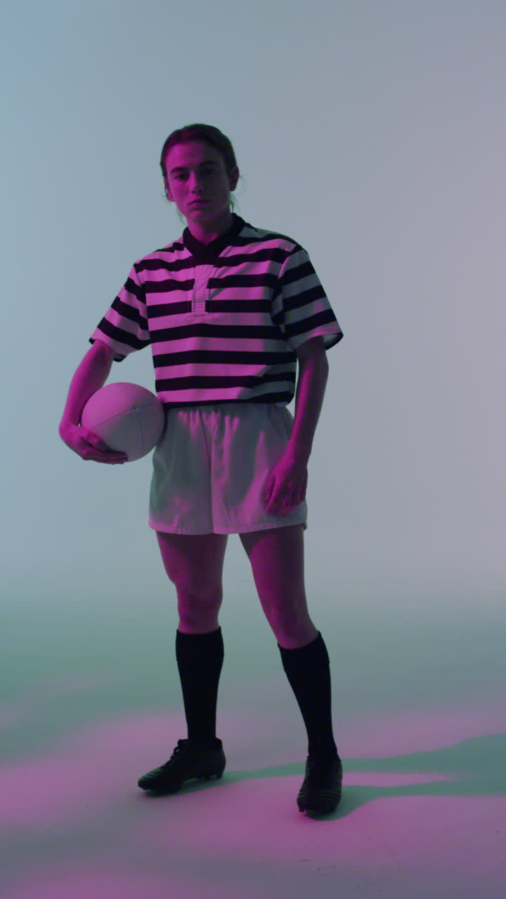 video vertical del retrato de una jugadora de rugby caucásica con una pelota de rugby sobre iluminación rosa neón