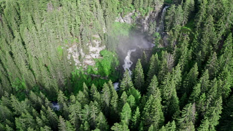 cascate del rutor waterfall hidden within dense green forest in the alps, aerial view