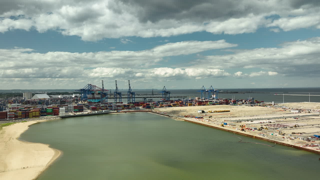 vista aérea del puerto de gdańsk, con grúas industriales, contenedores de envío y playa de stogi, que ilustra la intersección de la industria y la costa natural bajo un cielo nublado