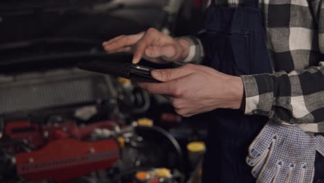 close-up-aufnahmen in zeitlupe von auto-service-technikern, die ein digitales tablet verwenden, um die fahrzeugprobleme zu untersuchen. autoreparatur, wartung, menschenkonzept.