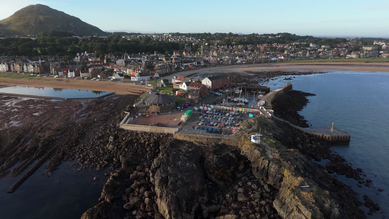 Aerial drone footage captures North Berwick, Scotland, in morning sunlight. views of the town’s historic harbour, sandy beaches, and rugged coastline along the North Sea