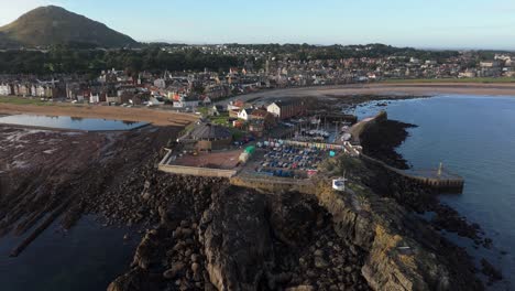 aerial drone footage captures north berwick, scotland, in morning sunlight. views of the town’s historic harbour, sandy beaches, and rugged coastline along the north sea