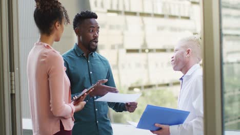 Diverse-business-people-discussing-with-tablet-and-documents-in-creative-office