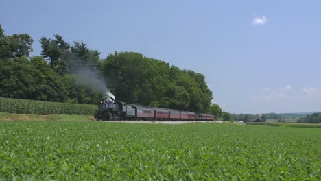 A-1924-Steam-Engine-with-Passenger-Train-Puffing-Smoke-Traveling-Along-the-Amish-Countryside-on-a-Summer-Day