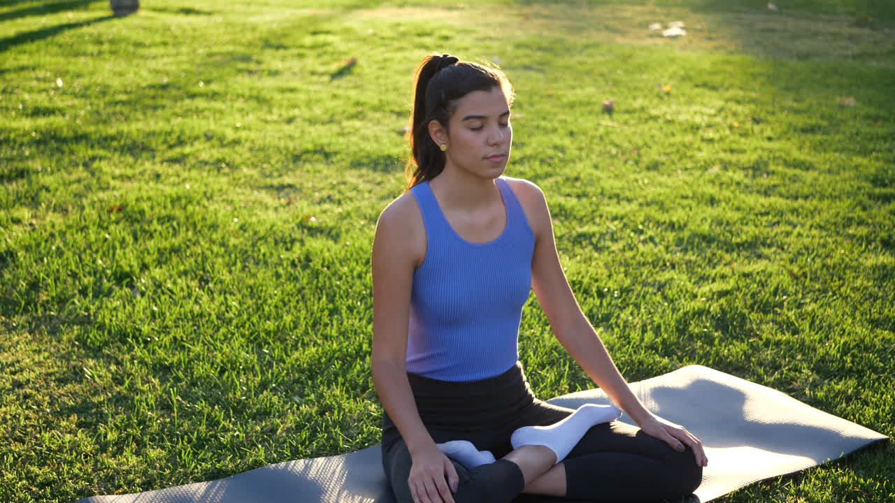 una joven en forma sentada en la posición del loto meditando en el parque al amanecer para mejorar su salud mental y relajarse