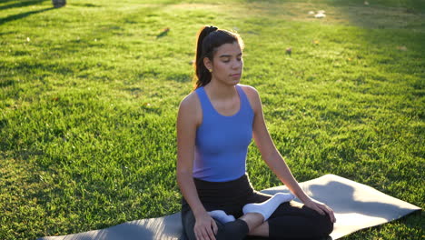 a fit young woman sitting in lotus position meditating in the park at sunrise to improve her mental health and relax