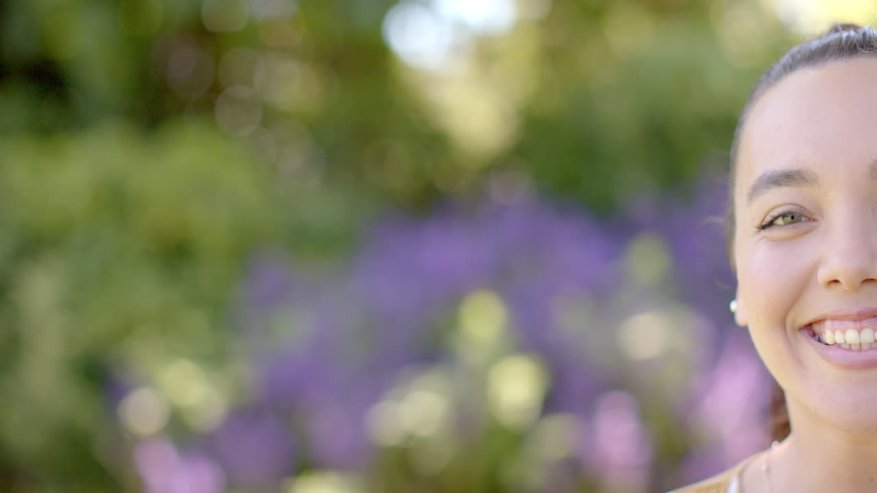 Smiling woman outdoors with blurred purple flowers in background, enjoying nature, copy space
