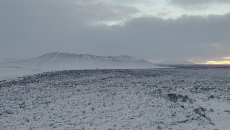 ascending aerial shot of majestic hverfjall crater covered with ice and snow during mystic foggy day