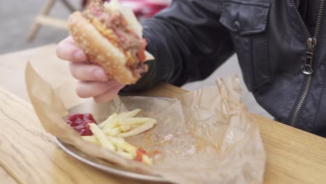 closeup view of man's hands holding big tasty burger. man with beard in the street cafe biting tasty big burger with cheese. french fries on the plate. shot in 4k