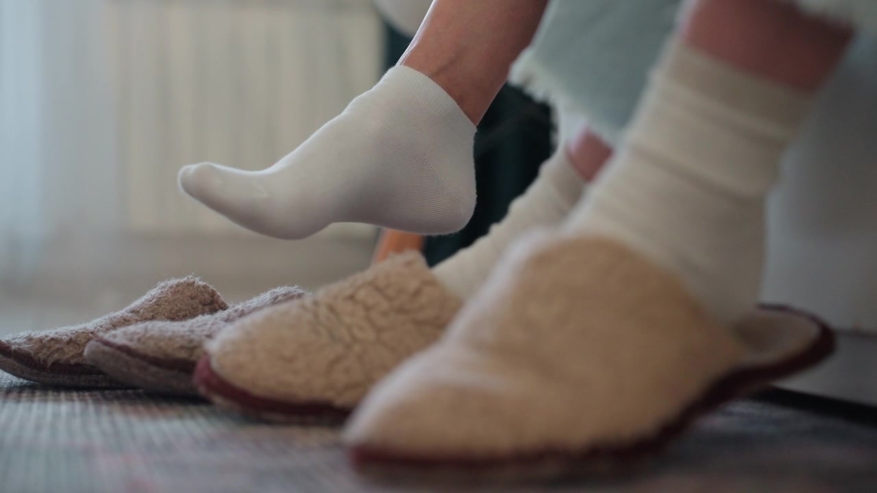 Piedi in calzini in una casa accogliente, studente e tutor seduti su un tappeto per una lezione di grammatica. Pantofole allineate vicino alla sedia, luce solare soffusa che filtra attraverso le tende. Un sottile movimento del piede indica un coaching rilassato e un'atmosfera calda.