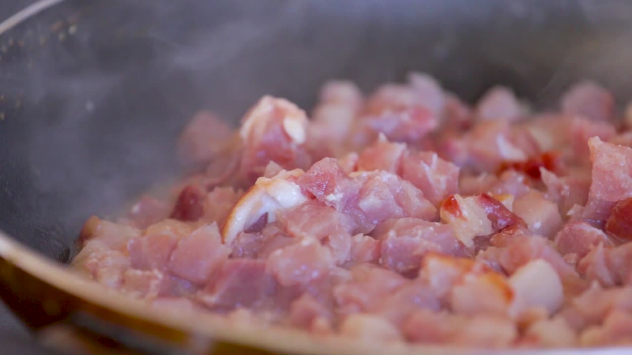 Bacon busy frying in a pan and also gets stirred