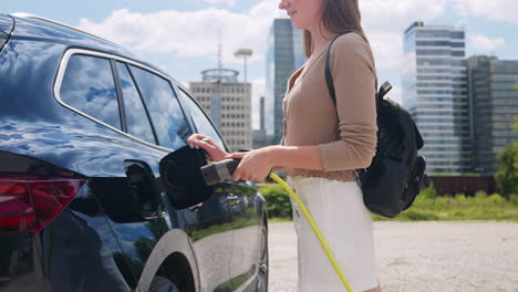 mujer poniendo un cargador en un coche eléctrico, alejándose a un centro de la ciudad, portátil