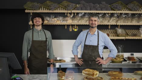 retrato de padre e hijo felices, dueños de negocios familiares, cinco en su panadería, mirando a la cámara y sonriendo