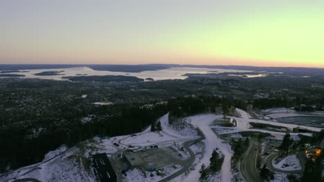 oslo city drone pull back with norwegian sea in background, vinterpark winterpark tryvann past ski jump holmenkollen, with nordic cross country skiing at sunset