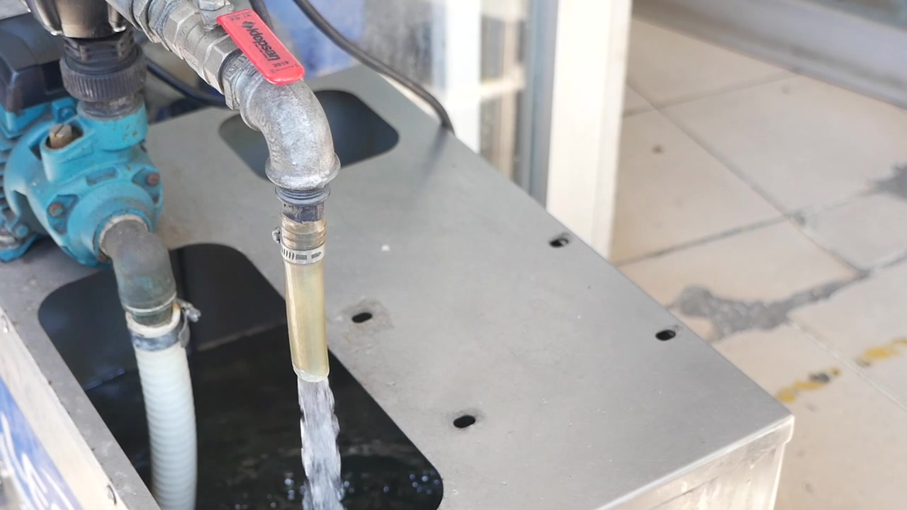 Acqua che scorre da un tubo in un contenitore con una pompa industriale.