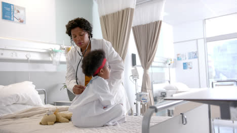 African-american-female-doctor-examining-girl-using-stethoscope-in-hospital-room,-slow-motion