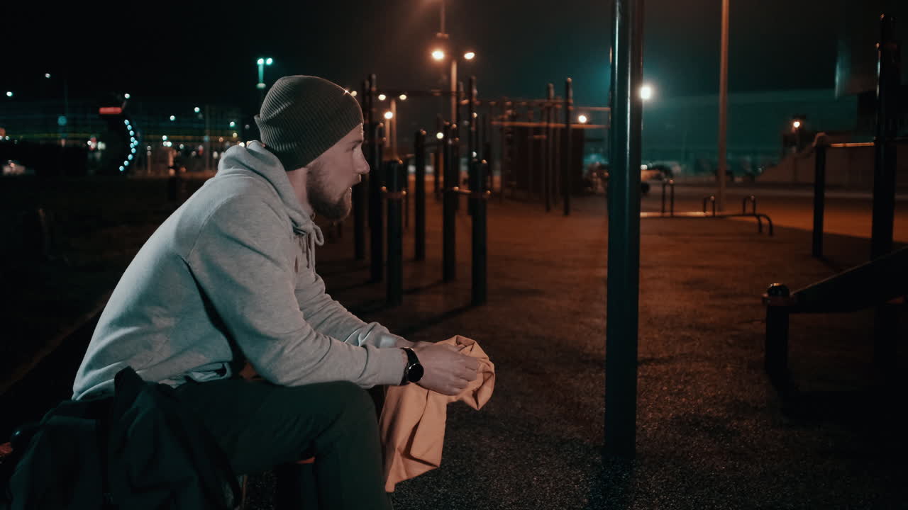 человек отдыхает после тренировки в открытом тренажерном зале ночью