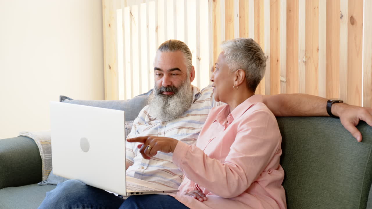 Using laptop, senior couple sitting on couch and smiling together