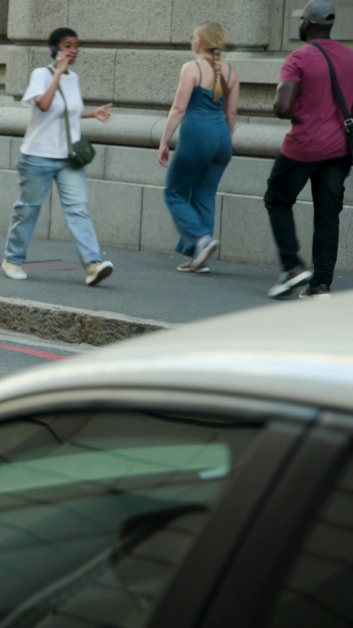 Vertical video: Crossing street, woman in black top khaki pants stepping onto sidewalk, passing car