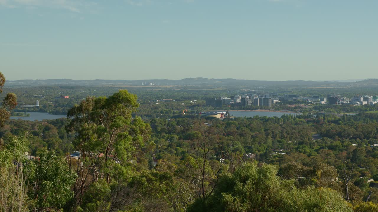 A panoramic view of Canberra’s CBD positioned to the right, with distant suburbs stretching toward the horizon, showing the city’s blend of urban and residential areas.