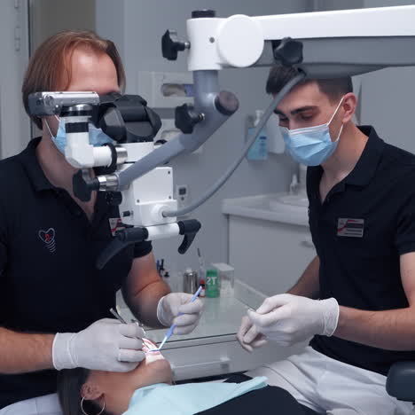 man dentist uses contemporary equipment. professional doctor treating patient's teeth through the microscope in dental office. specialist and his assistant in clinic.