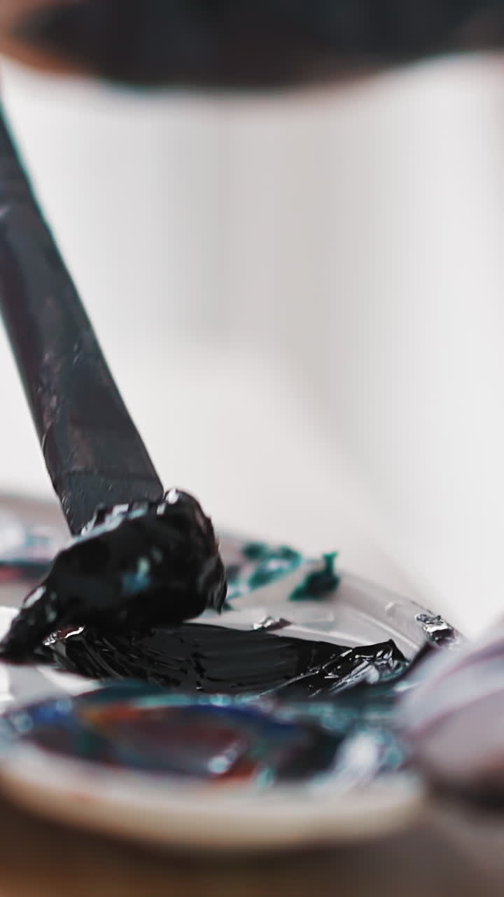 Professional woman artist takes dark blue paint with brush from white plastic palette at modern wooden easel in studio extreme closeup slow motion