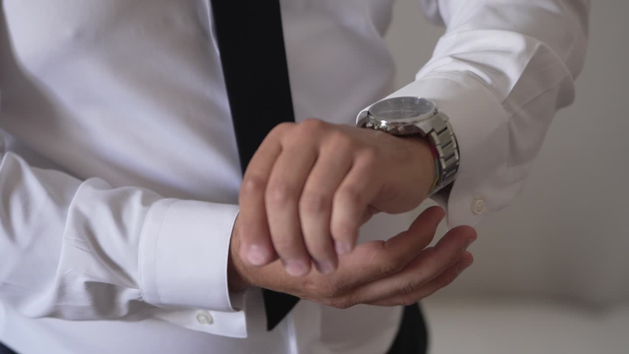 Close up of groom in white shirt and tie adjusting silver wristwatch