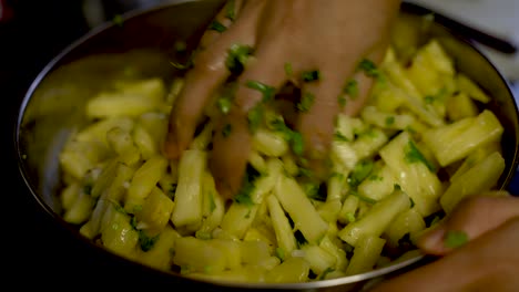 diced pineapple pieces being mixed with cilantro, salt and green chillies in metal bowl