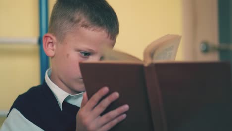 sad-boy-turns-pages-of-textbook-preparing-for-exams-at-home