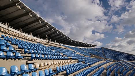 rows of empty blue and beige stadium seats create a wave like pattern beneath a cloudy sky, evoking feelings of anticipation and the vastness of an open air venue