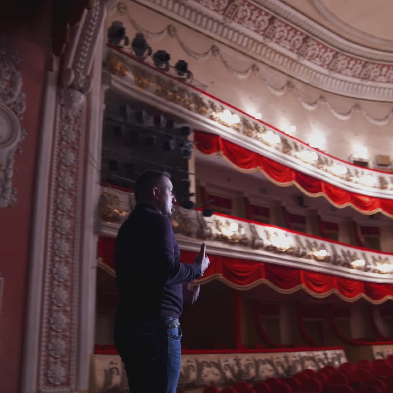 Actor in front of empty theatre hall. Man is standing on stage and talking with gestures before the performance.