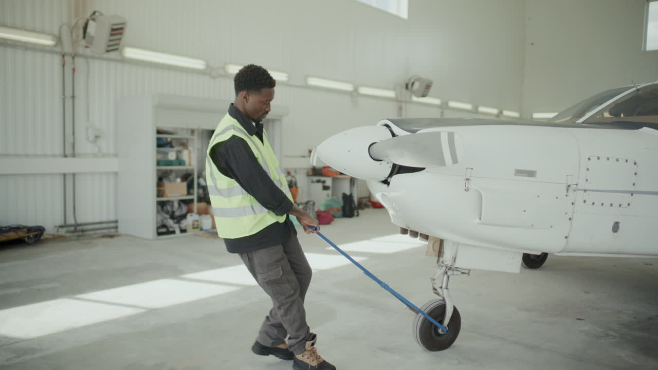 African American Worker Pulling Light Aircraft Manually in Hangar