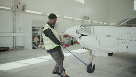 african american worker pulling light aircraft manually in hangar