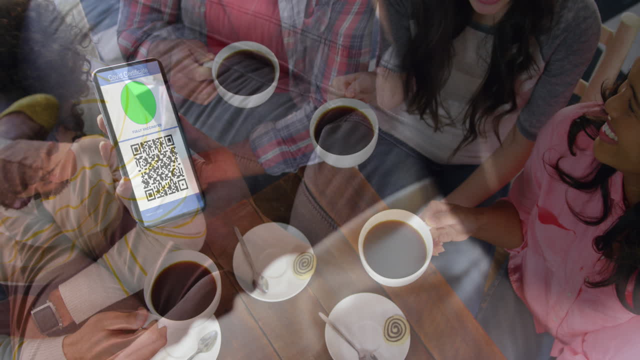 mujer sosteniendo un teléfono inteligente con código qr en la pantalla contra un grupo de amigos tomando café juntos