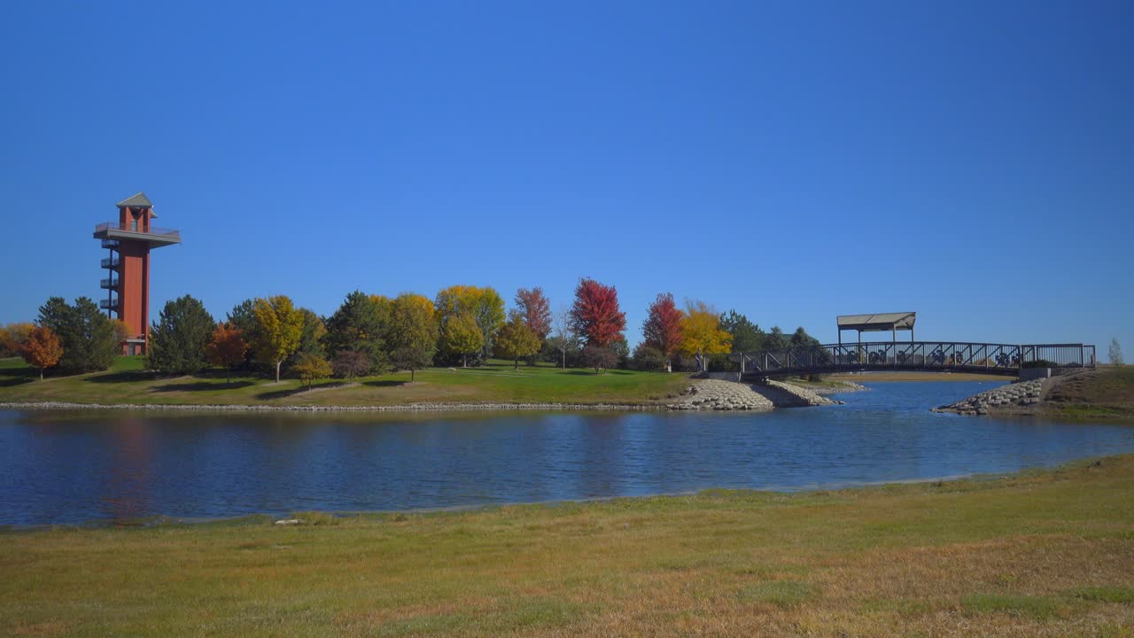 caminando a través de un puente sobre un estanque en un parque de la ciudad con una torre de vigilancia