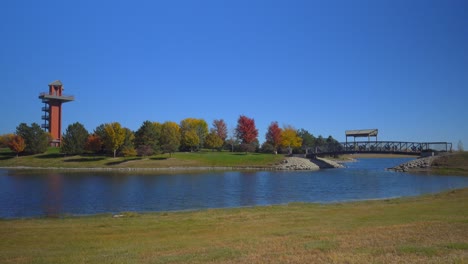 Walking-across-a-bridge-over-a-pond-at-a-city-park-with-a-watchtower